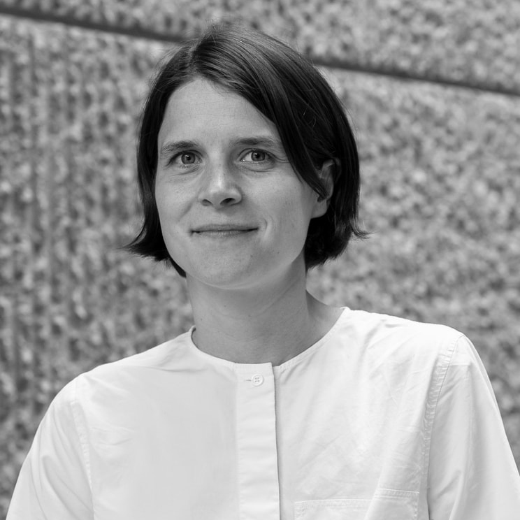 Black-and-white headshot of UVA School of Architecture alumna Violette de la Selle wearing a light-colored shirt, standing in front of a textured stone wall.