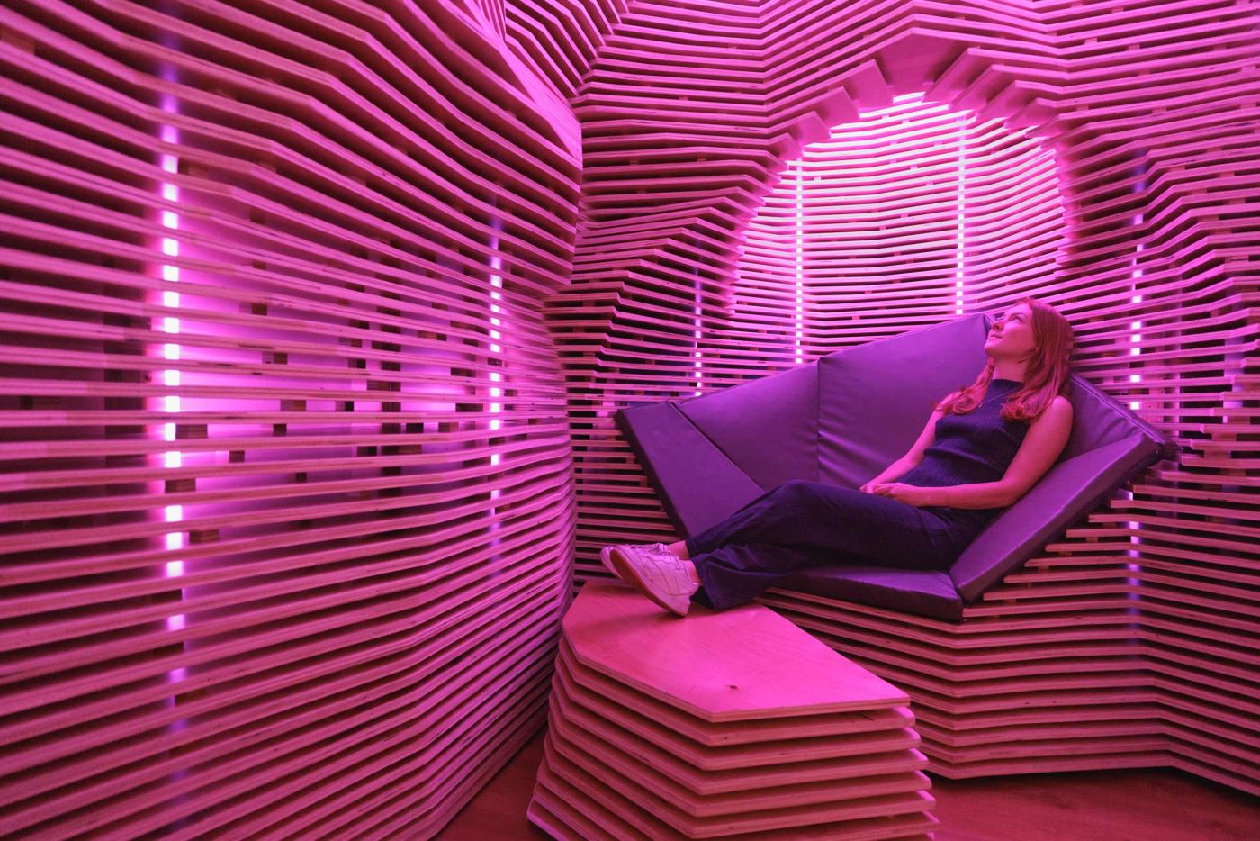 Student lying down and relaxing in wood installation with pink lighting