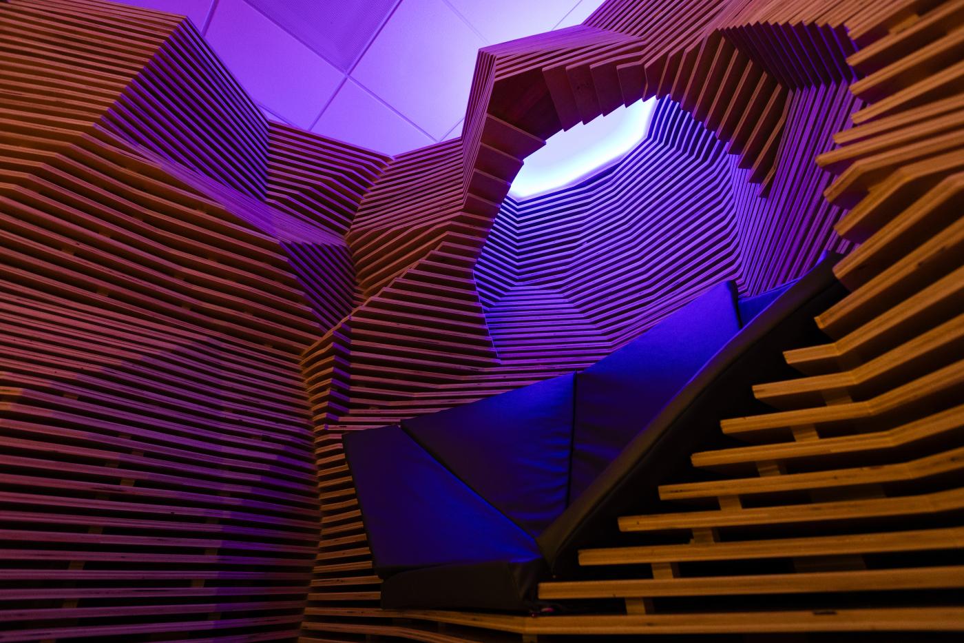Wood installation and seating area called Reflection Room with purple mood lighting
