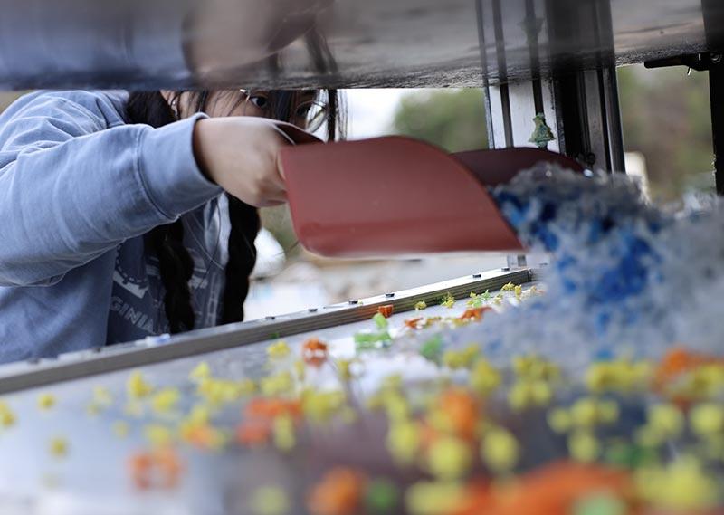 colorful bits of yellow, orange and blue plastic scraps being scooped onto heated surface