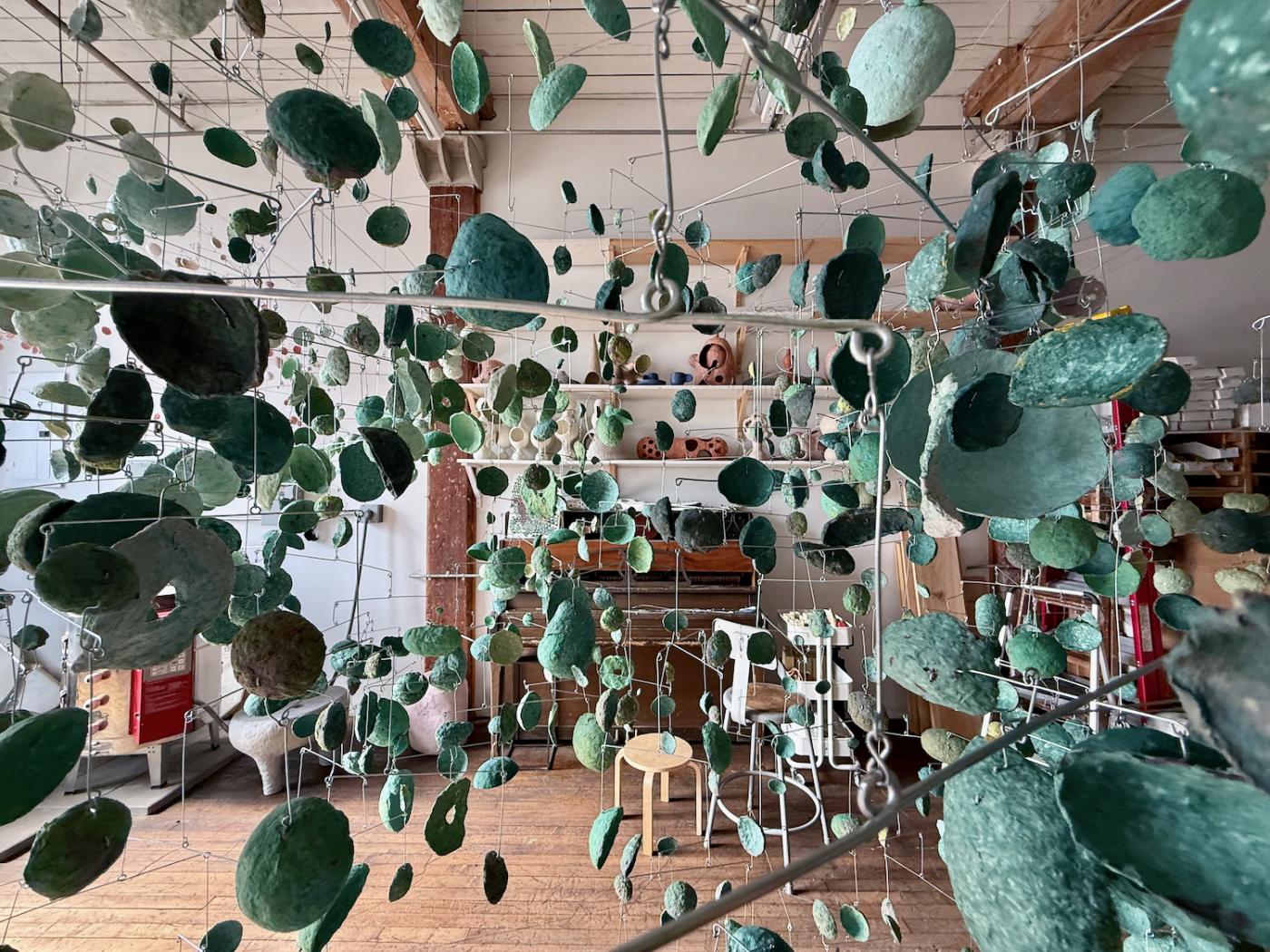 A dense cluster of hanging mobiles made in abstract green forms