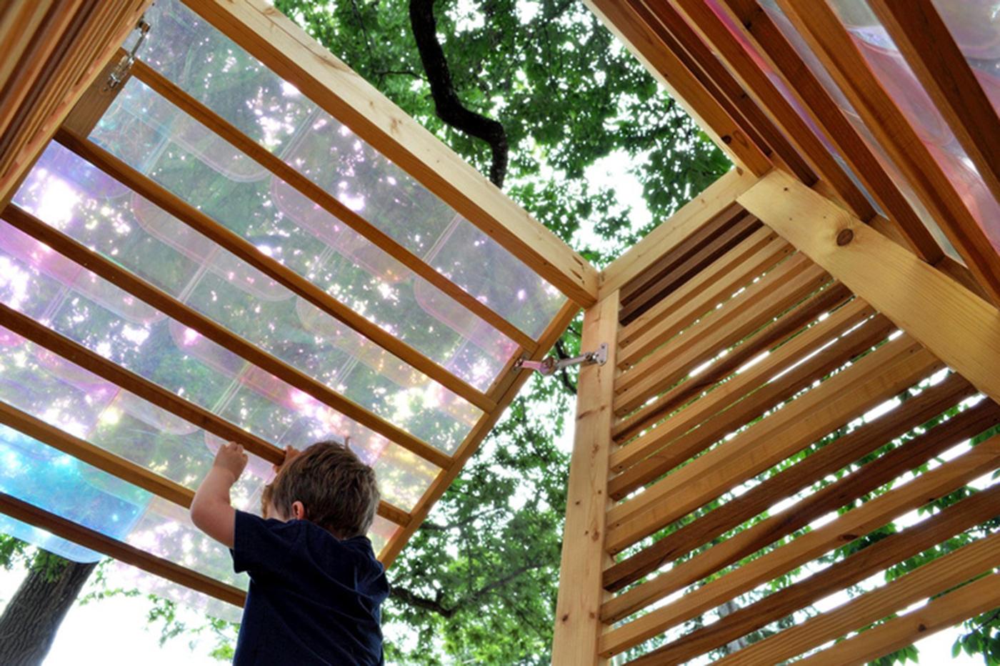 child pushes open an outdoor structure made of wood and colorful plastic
