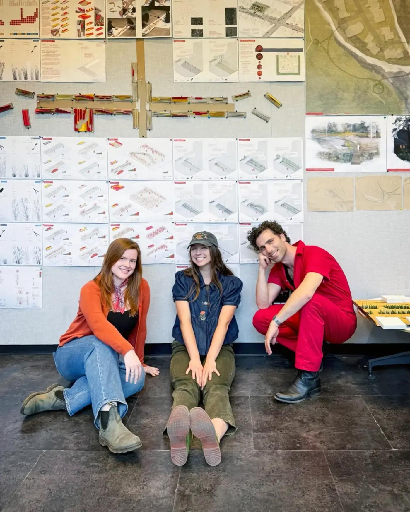 Three students seated in front of their pinned up design work.
