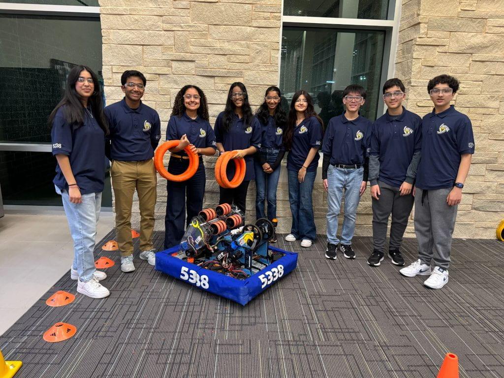 High school robotics team students stand in a line behind their custom built robot.